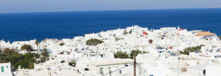 Happy women standing on the promenade and looking away, pointing at beautiful cityscape of Mykonos .Copy space